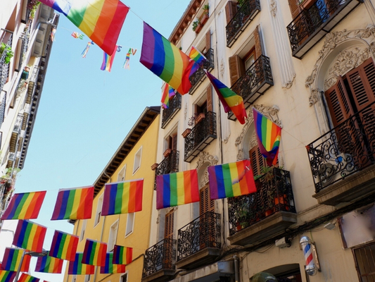 Rainbow flags hanging between classical buildings in Chueca neighborhood during gay pride month downtown Madrid, Spain