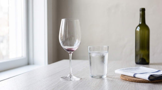 Empty wine glass beside a glass of water in morning light, with a wine bottle in the background, representing moderation