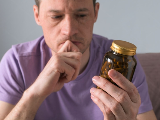 Why male enhancement supplements fail: Machismo Plus guide showing a thoughtful man examining a supplement bottle and questioning whether the formula is working